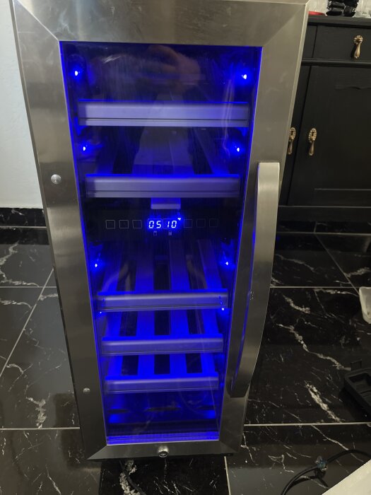 Vinkyl med blå belysning på svart marmorgolv i modernt kök.