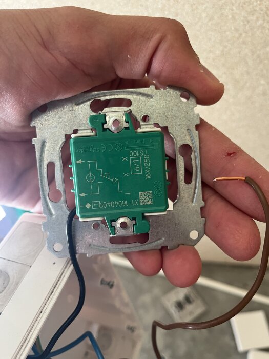 Närbild på en hand som håller en öppen strömbrytare med en lös brun kabel. En blå kabel syns också inkopplad.