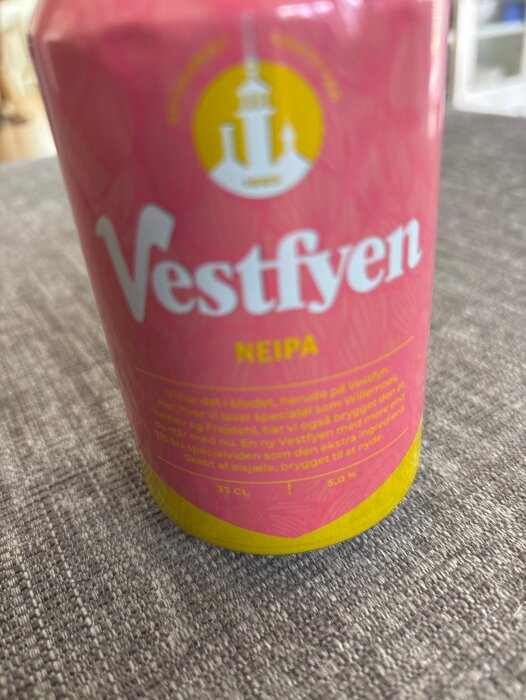 Burk med Vestfyen NEIPA på grått underlag. Etikett i rosa och gult med text om innehåll och bryggning.