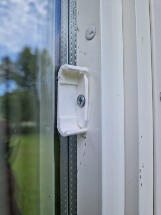 Vit spröjsfäste med skruv på ett Tiivi-fönster från 2006-2008 i närbild. Fästet visar tecken på slitage.