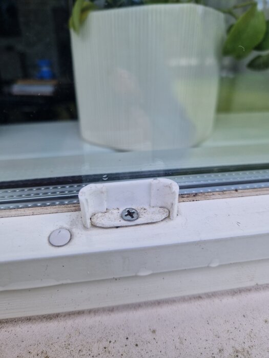 Spröjsfäste på ett Tiivi-fönster från 2006-2008, med en vit skruv och en krukväxt i bakgrunden.