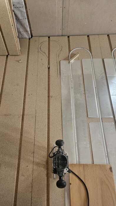 Spånskiva med frästa spår och ritad kontur för rördragning, samt verktyg för fräsning.