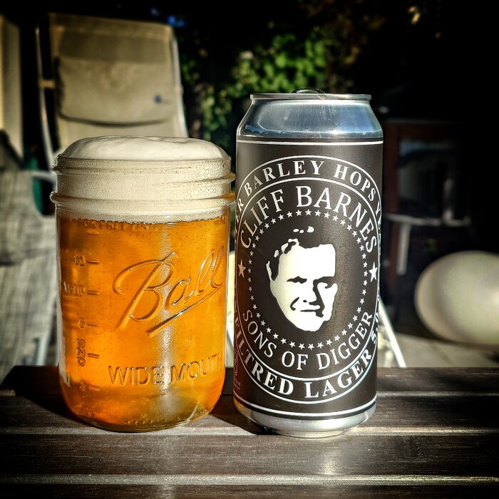 En burk Cliff Barnes ofiltrerad lager och ett glas öl på bord i solljus.