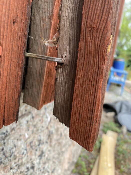 Närbild av lockläkt med träkil på undersidan, fastsatt med en spik i en gammal träfasad på en gård.