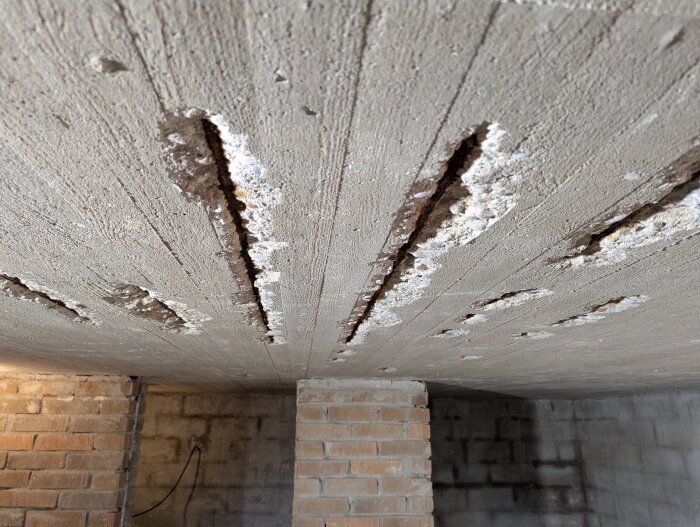 Sprucken betongplatta i garagegolv med exponerad rostig armering. Vissa delar av betongen har ramlat av, och de rostiga armeringsjärnen syns tydligt.
