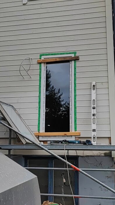 Arbete pågår med att installera en ny dörrkarm och isolering på en fasad, med säkerhetsglas och verktyg i närheten.