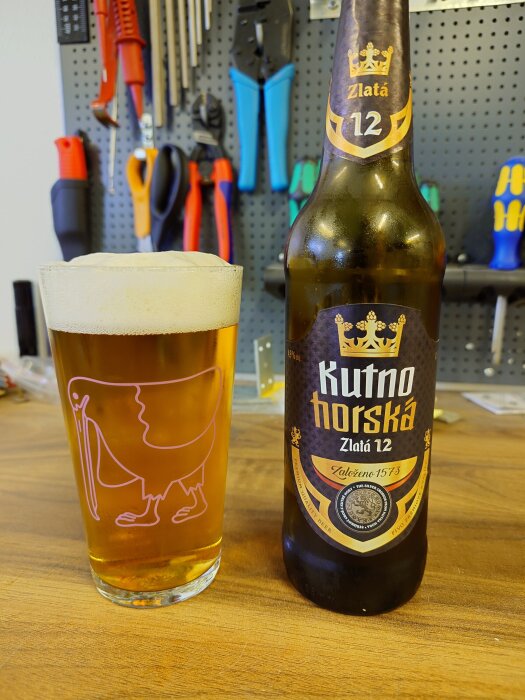 En flaska Kutno Horská ölmärke och ett fullt glas öl på en arbetsbänk med verktyg i bakgrunden.