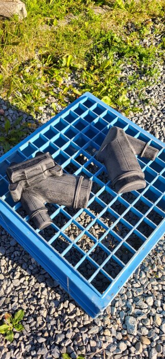 Svarta gjutstycken placerade på ett blått rutnät på marken, omgivna av grus och gräs.