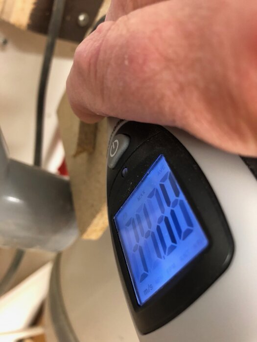 Anemometer-mätare visar 33,98 m/s, hålls över en rörkoppling i ett centralt dammsugarsystem, närbild.