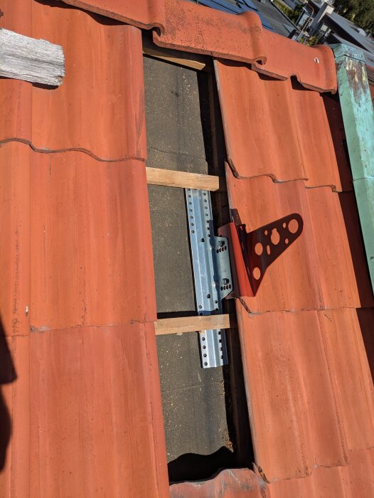 Rött tegeltak med delvis avlägsnade pannor visar början av installationen av ett nockräcke.