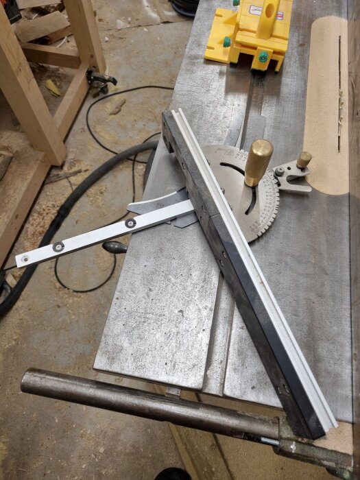 Justerbar såglinje på arbetsbord med skjutmått och gjutjärnsstång, oskärpat aluminium, gjutjärn och synliga justerbrickor.