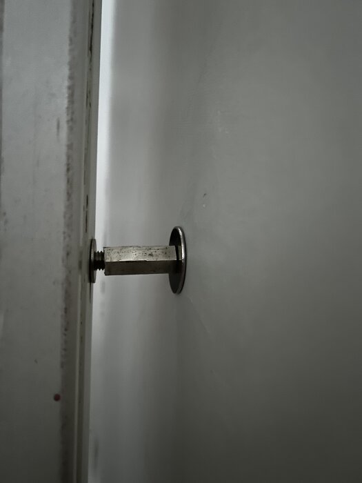 Vägg med fastsatt metallskruv och distansbricka i närbild.