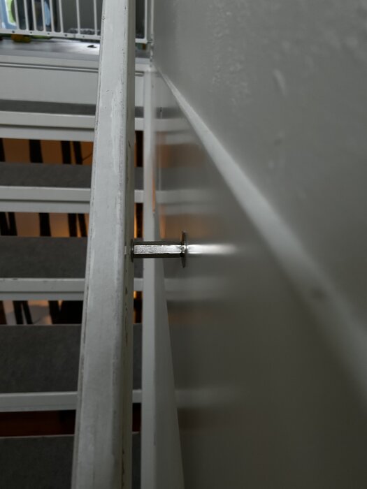 Ledstångsskruv och distansmontering på vägg vid trappa, skruven sticker ut från väggen med en distansring.