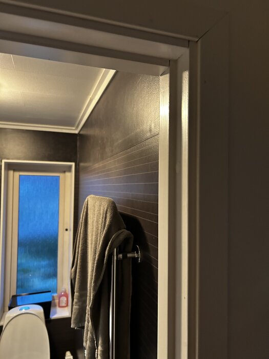 Badrumsvägg med handdukshängare, handduk och en del av ett fönster i bakgrunden.