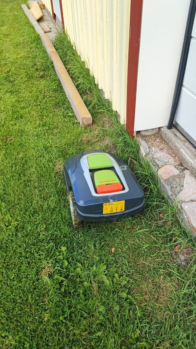 Robotgräsklippare nära vägg med trästolpar bredvid; försöker undvika stopp vid gränskabel enligt forumdiskussion.
