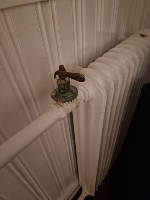Radiator med en gammal ventil i ett hem, troligen för att justera vattenflödet. Synlig detalj av ventilen och väggen bakom.