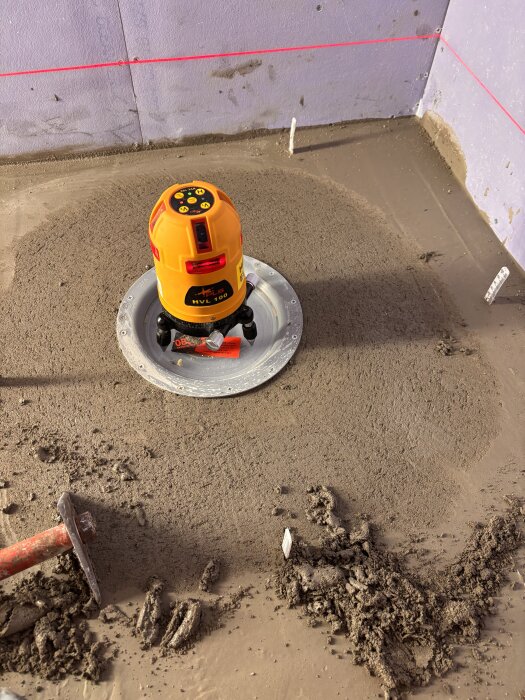 Laserverktyg och flytspacklad yta i ett bygge där första lagret spackel har applicerats. Lasernivå och ojämn spackling syns tydligt.