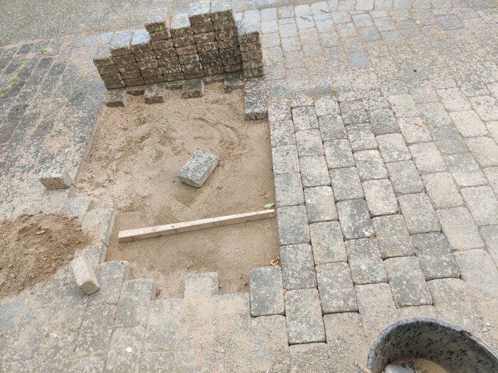 Paving stones reinstalled after water pipe replacement, partially completed with sand, bricks, and a leveling bar visible.