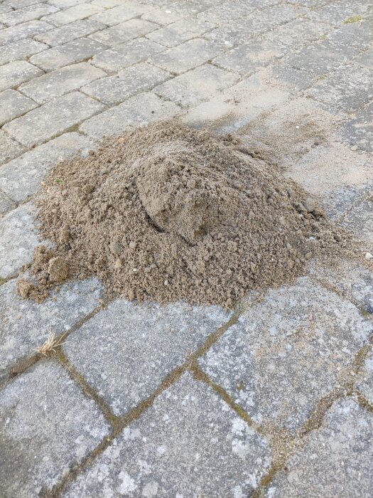 Hög med sand och jord på stengång, del av arbete med att återställa marken efter vattenledningsbyte vid entré.