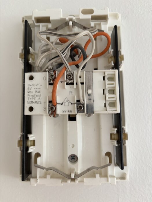 Elektrisk dörrklocka med synliga kopplingskablar och märkningar för spänning och effekt, däribland 8-16V och max 15W, installerad på vägg.