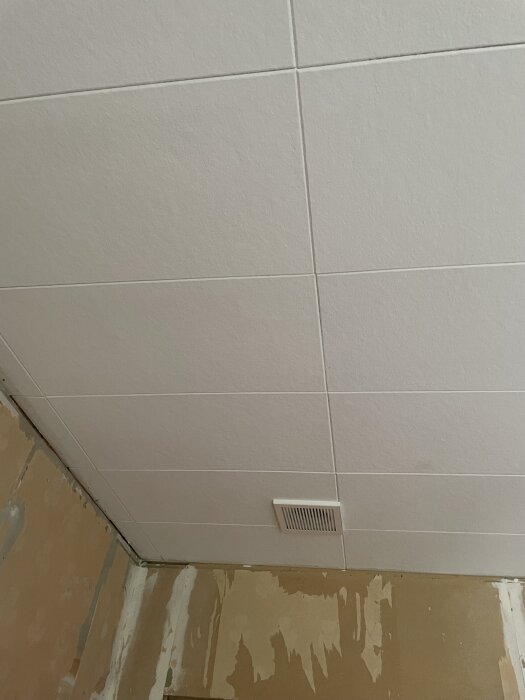 Tak med vita plattor och en ventil, vägg under renovering.