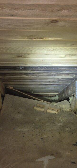 Svarta plankor på kallvinden med antydan till mögel, eventuellt tecken på fuktskada; utredning om läcka pågår.