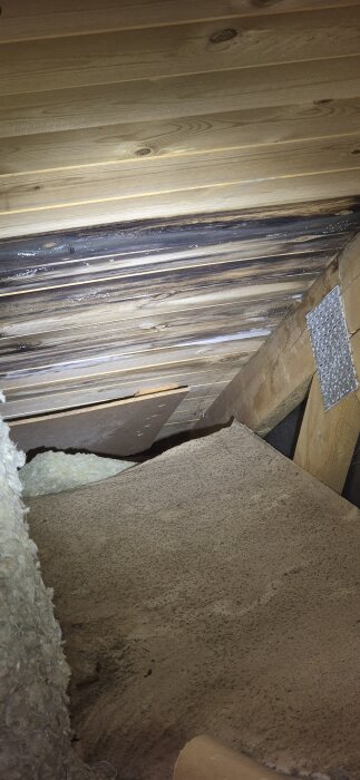 Svartfärgade plankor på en kallvind med möjlig fuktskada, synliga träbjälkar och isolering nära taket.