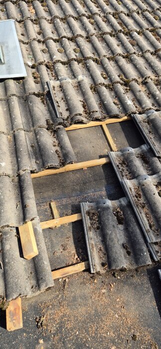Bild visar ett tegeltak med öppna partier, några takpannor borttagna för inspektion, synligt trä och misstänkt område med svarta plankor.