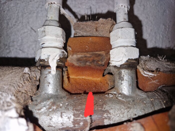 Två rör med ventiler och isolering, ett rött märke under tyder på plats för vattencirkulation till radiator.