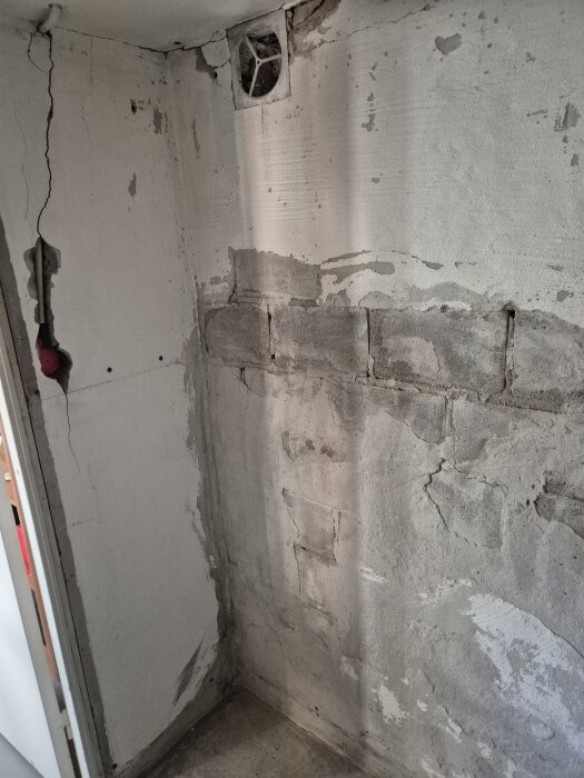 Sprucken källarvägg med synliga ventilationshål och trasig puts visar tidigare bastuinstallation som nu är riven; sprickor och slitage syns tydligt.
