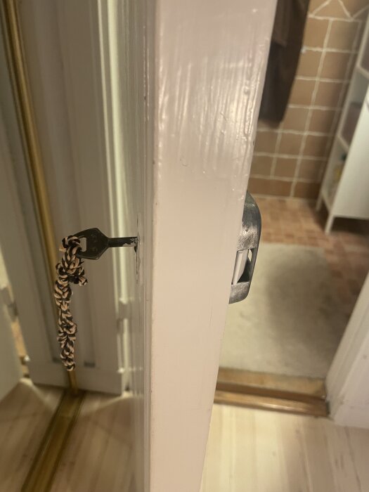 En gammal badrumsdörr med nyckel hängande i ett nyckelhål, utan handtag eller vred på insidan.