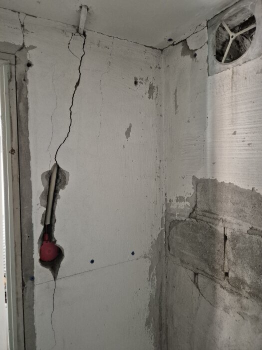 Sprucken vägg i källare med synlig spricka vid ventil och elsystem, spår av reparationer; vägg gjord av porös, blåfärgad betong.