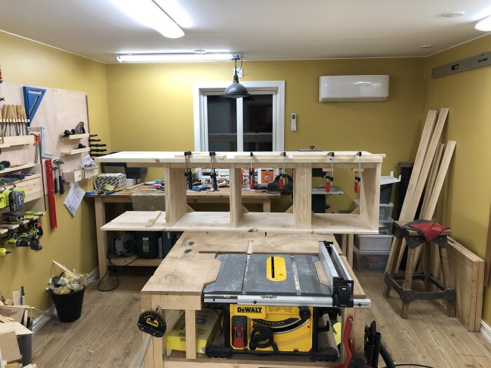 Verkstadsmiljö med en del av en träkonstruktion i processen att byggas, tvingar används för att hålla ihop delarna.