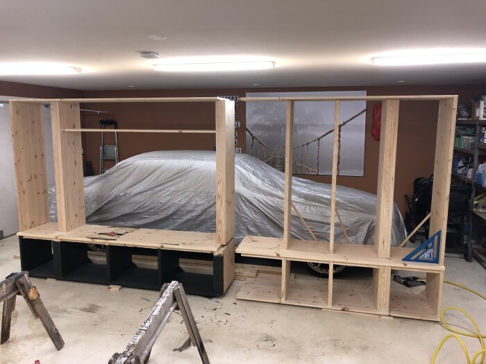 Trästomme av byggd platshylla under konstruktion i ett garage, med en täckt bil i bakgrunden och verktyg synliga på golvet.