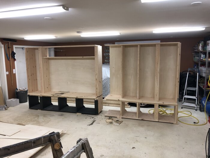 Bygge av trähylla i färdiga sektioner i ett garage, med öppna fack och träramar för TV och förvaring.