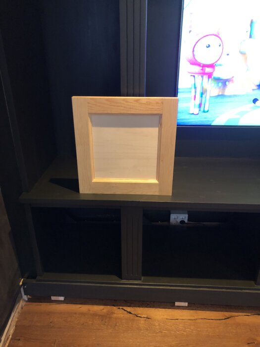 Träpanel tillverkad av furu och poppelplywood visas framför en grönmålad platsbyggd hylla med en del av en TV i bakgrunden.