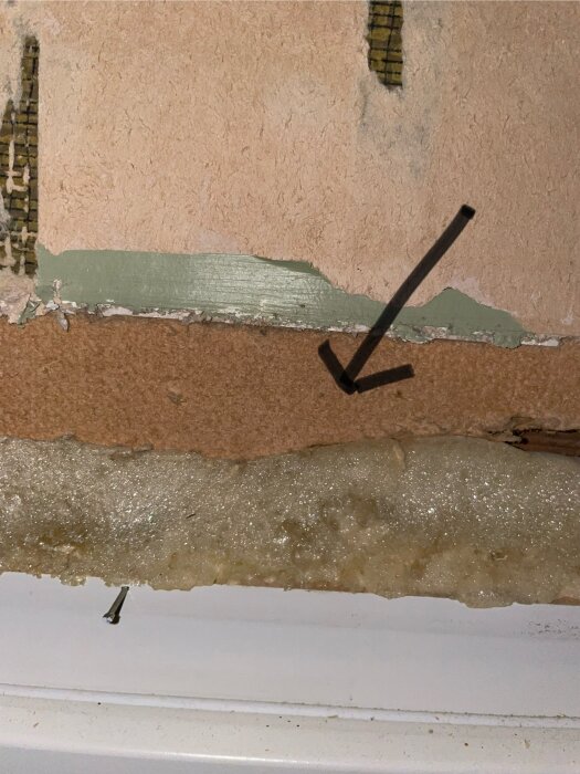 Vägg med avskalad tapet, exponerad Tretex-liknande skiva och isoleringsmaterial, samt en pil som pekar mot det exponerade området.
