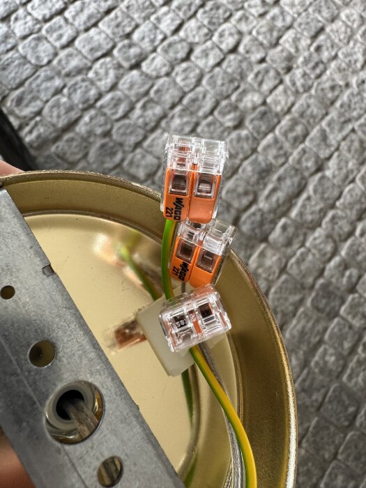 Två orangefärgade WAGO-kontakter på en guldmetallic platta, kopplade med grön och gul kabel.