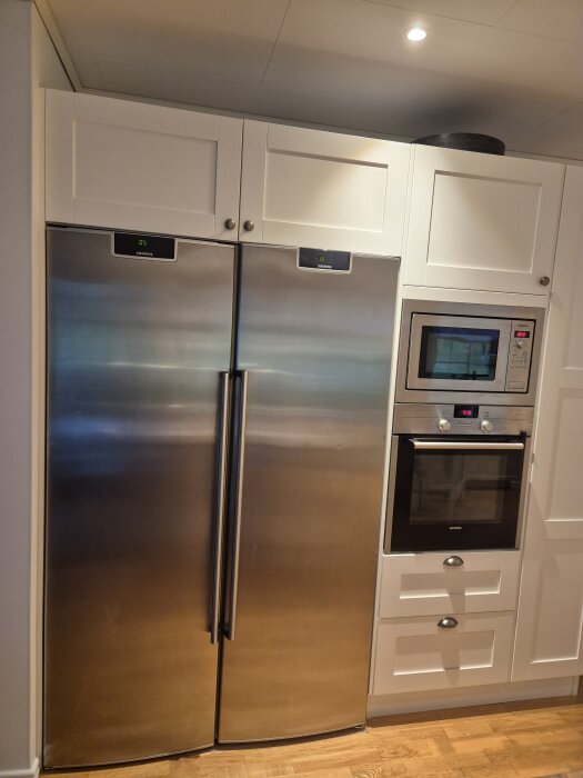 Inbyggt kyl- och frysskåp i rostfritt stål från Siemens, installerat i köksnische, bredvid en integrerad ugn och mikrovågsugn i vita skåp.