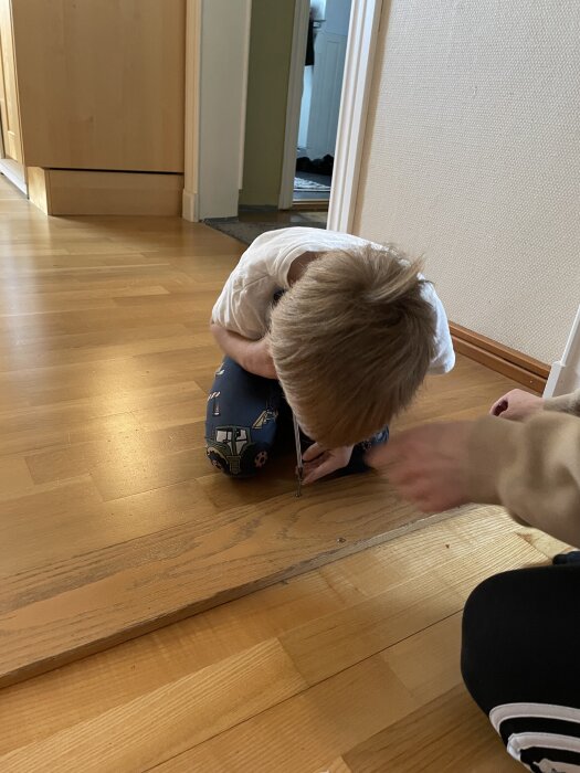 En person lossar golvplankor med en skruvmejsel på ett trägolv.