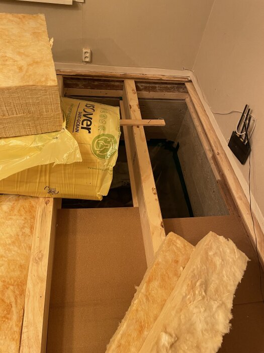 Byggplats med exponerad reglar och isolering; gula ISOVER-paket och glasfiberisolering på golvet vid renovering.