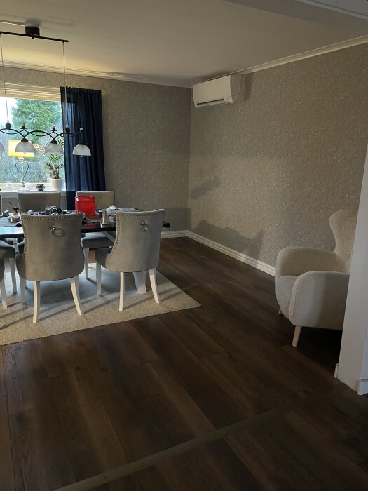 Renoverad matsal med mörkt trägolv, gråmålade väggar och modernt matbord med stolar. Väggmonterad AC och stilren taklampa.