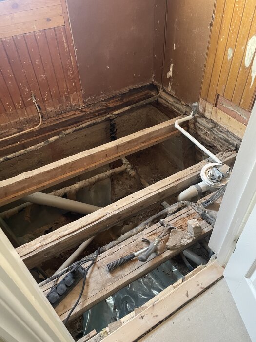 Renovering av badrum med borttagen golvyta, exponerade bärlinor och verktyg som hammare, i en entréhall eller toalettrum.