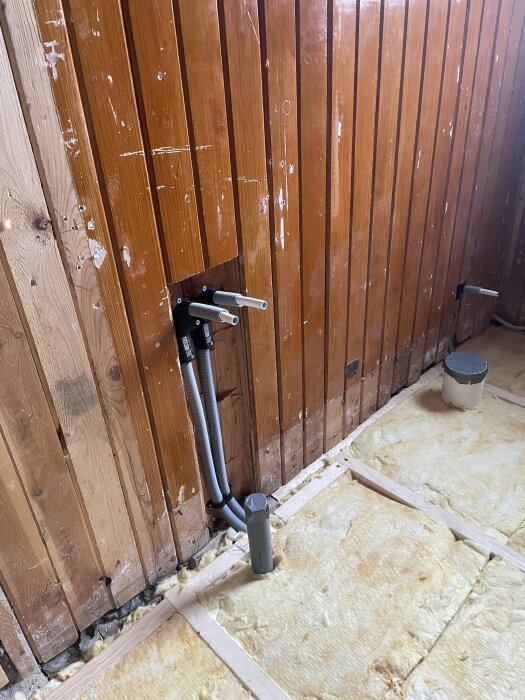 Vägg med nyinstallerade VVS-rör och isolering på golvet i samband med husrenovering.