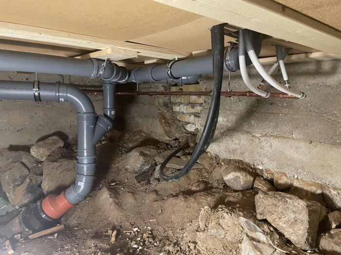 Nya VVS-rör under hus i byggprojekt, grå- och vitfärgade rör kopplade i jordig miljö, del av renovering och uppdatering av hela rörsystemet.