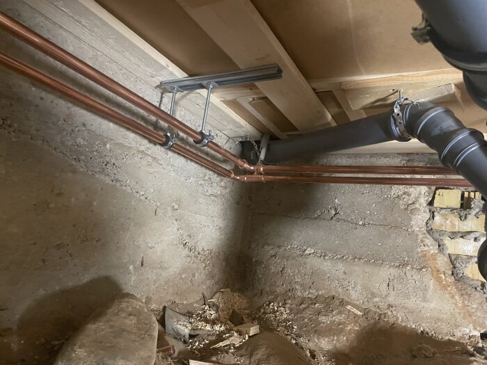 Nya kopparrör och avloppsrör installerade på vägg i källaren, visar uppdaterade VVS-arbeten.