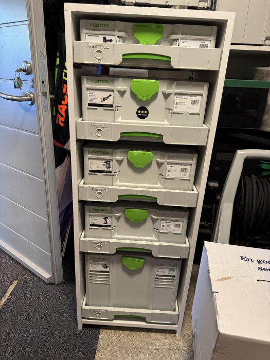 Festool Systainer-lådor organiserade i en vit hylla med grön- och gråfärgade detaljer i ett garage.