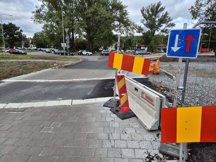 Vägskylt vid vägavstängning med pilar i motsatta riktningar, möjligen monterad upp och ner, omgiven av trafikbarriärer och vegetation.