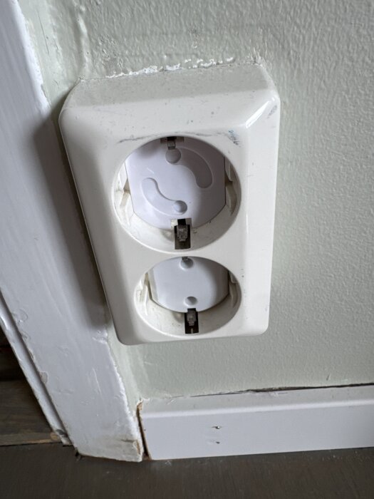 Dubbel vägguttag med uttagen blockerade av plastskydd mot ljus vägg.