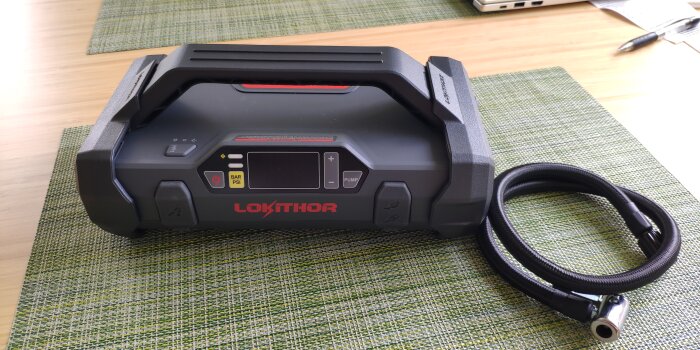 Portabel startbooster med kompressor på en grön bordstablett, bredvid en svart slang.